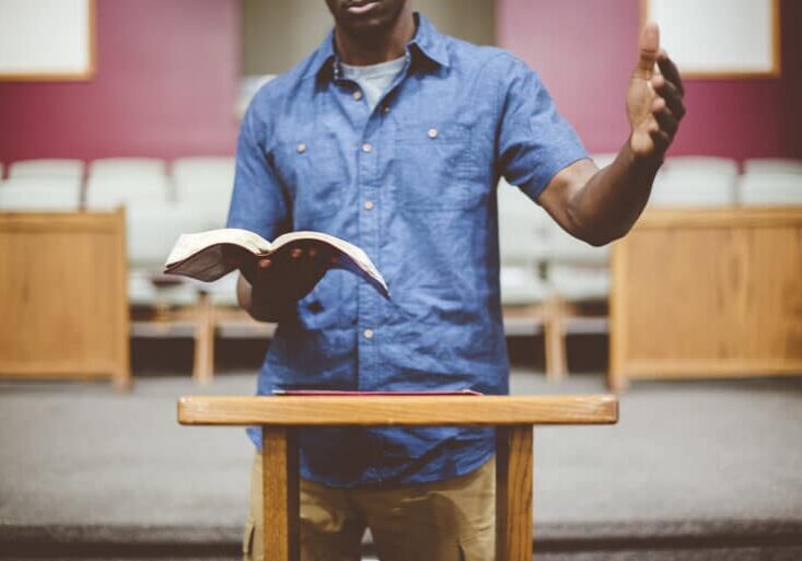 Closeup shot of a male reading the bible near a wooden stand with a blurred background
